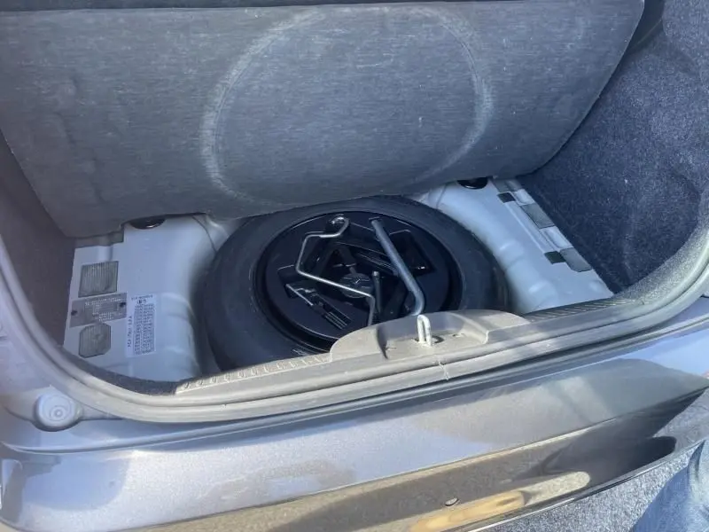 Coffre ouvert d'une Fiat 500 gris foncé 2019, vue sur la roue de secours et les outils de changement de pneu.