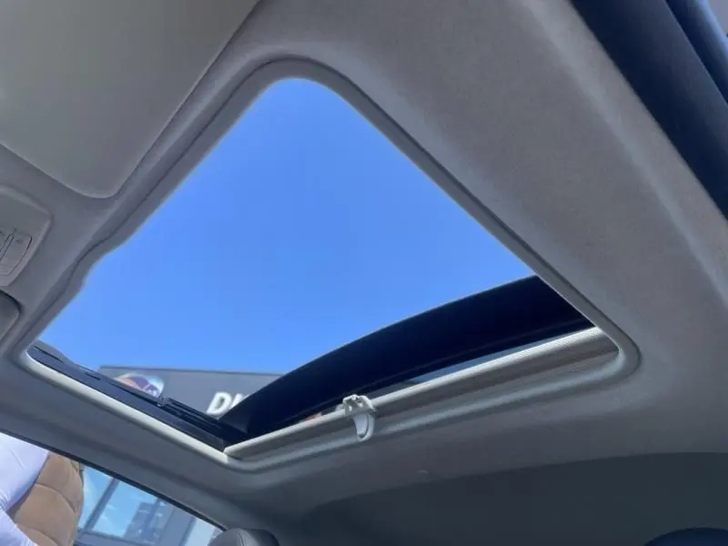 Toit ouvrant panoramique ouvert vu de l'intérieur d'une Fiat 500 gris foncé, ciel bleu visible à travers.