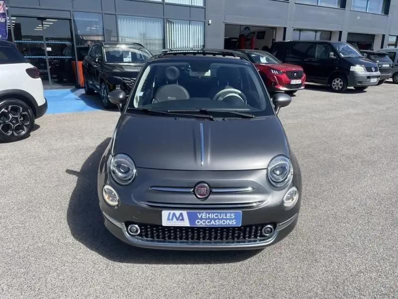 Vue avant d'une Fiat 500 gris foncé 2019 avec toit ouvrant, sur parking de véhicules d'occasion.