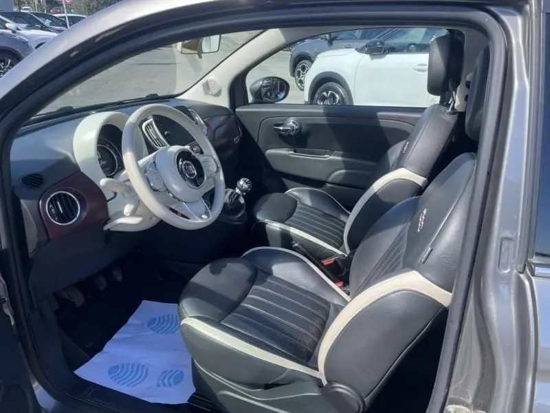 Vue intérieure côté conducteur de la Fiat 500 gris foncé 2019, avec volant blanc et sièges noirs à surpiqûres claires.