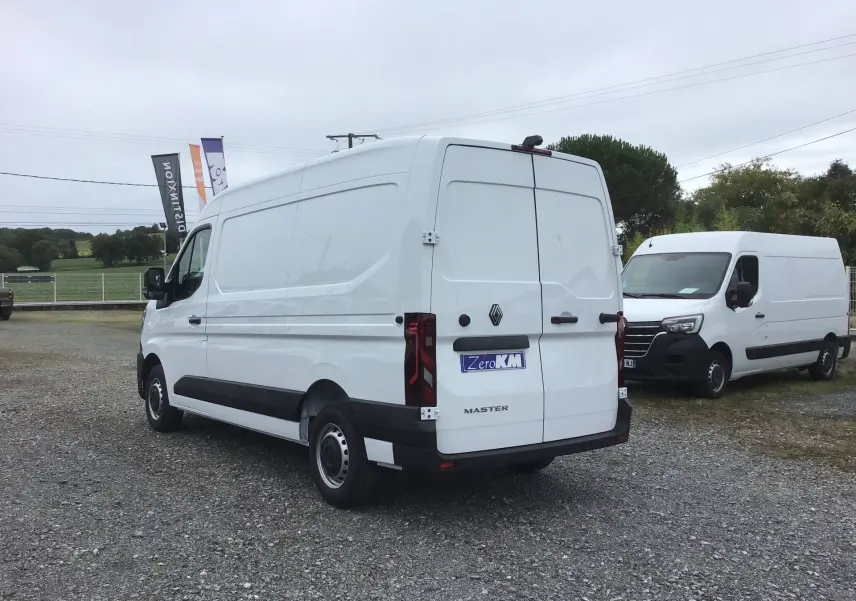 Renault Master blanc vue 3/4 arrière droit, fourgon utilitaire avec feux arrière verticaux et bandeau noir bas de caisse.