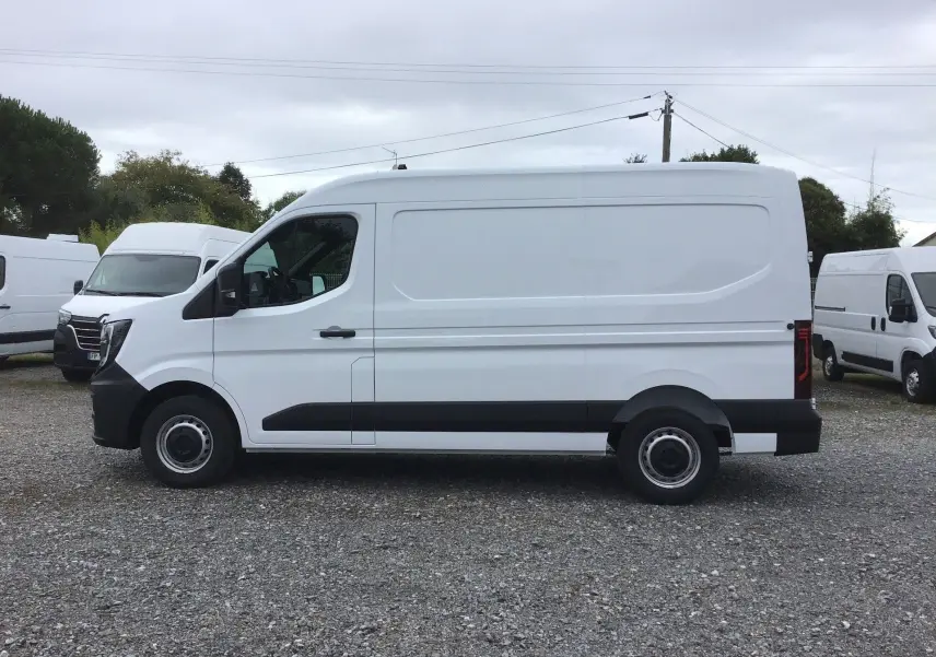 Vue de profil côté gauche d’un Renault Master blanc L2H2 2025 avec bandeau noir sur bas de caisse, stationné sur sol gravillonné.