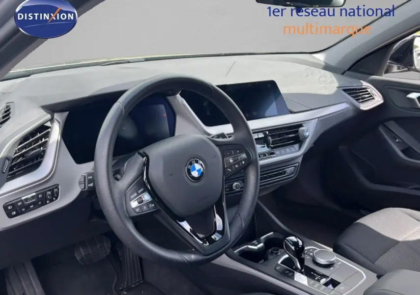 Intérieur BMW Série 1 116i 2022 vu côté conducteur, volant cuir noir et tableau de bord moderne gris foncé.