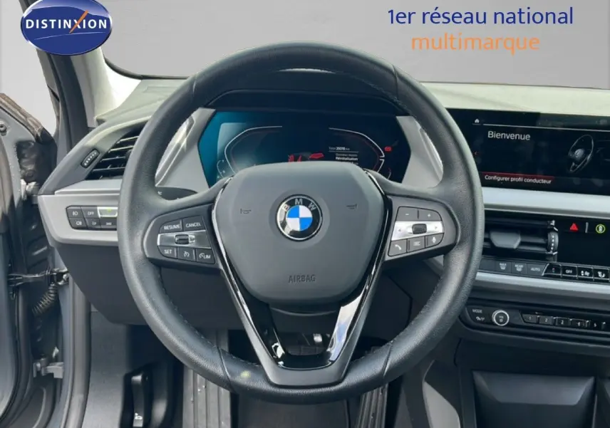Vue intérieure centrée sur le volant noir d’une BMW Série 1 116i 2022 avec tableau de bord numérique et écran tactile.