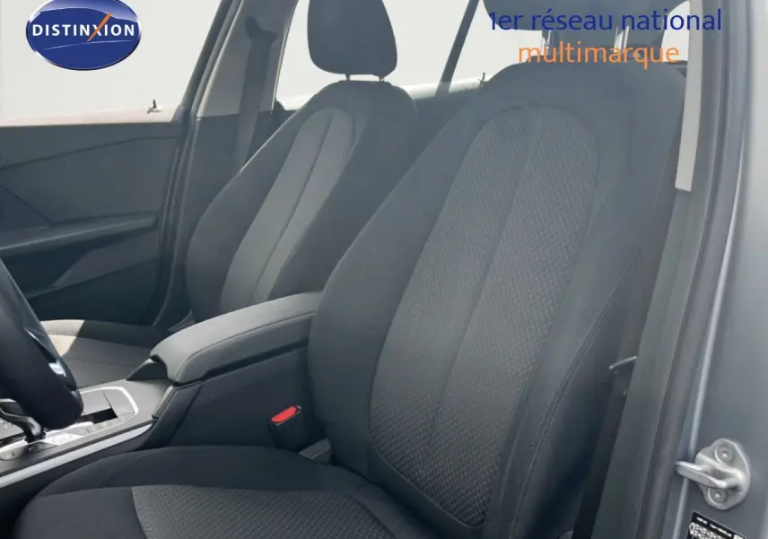 Vue intérieure côté conducteur de la BMW Série 1 116i 2022 avec sièges tissu gris foncé et accoudoir central.