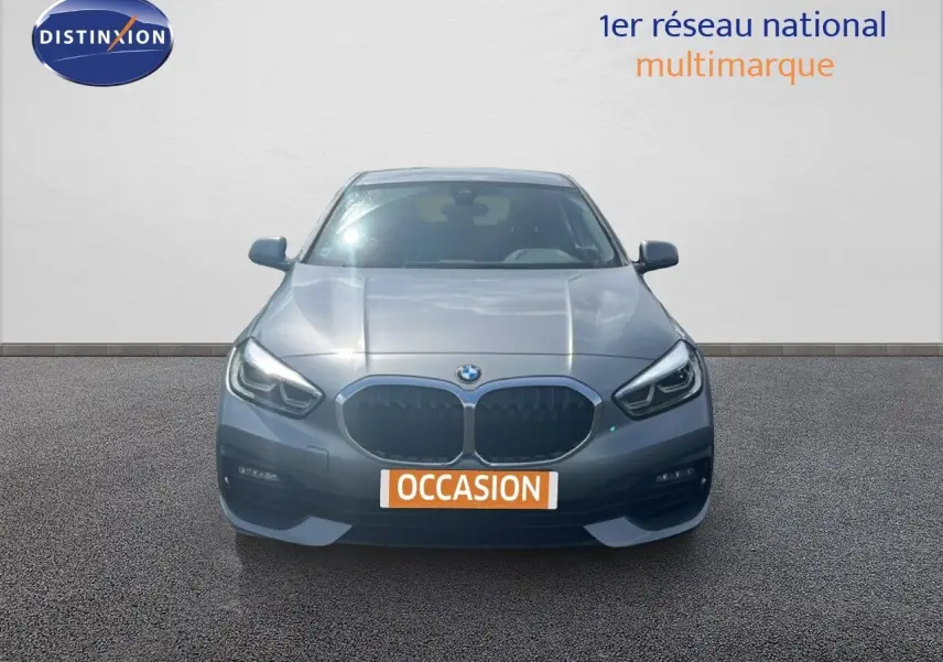 BMW Série 1 116i gris Frozen Pure Grey vue de face, avec calandre double haricot et phares LED allumés.