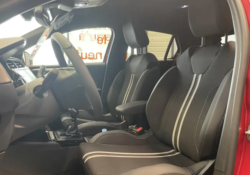 Vue intérieure côté conducteur de l'Opel Corsa rouge 2026, sièges sport noirs avec bandes blanches et volant cuir.