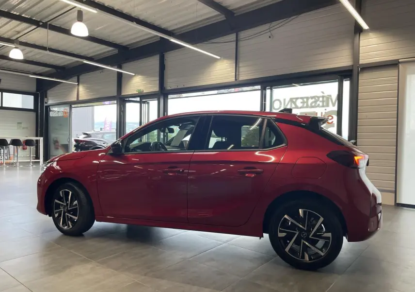 Opel Corsa rouge vue de profil côté gauche, avec jantes alliage et toit noir en showroom lumineux.