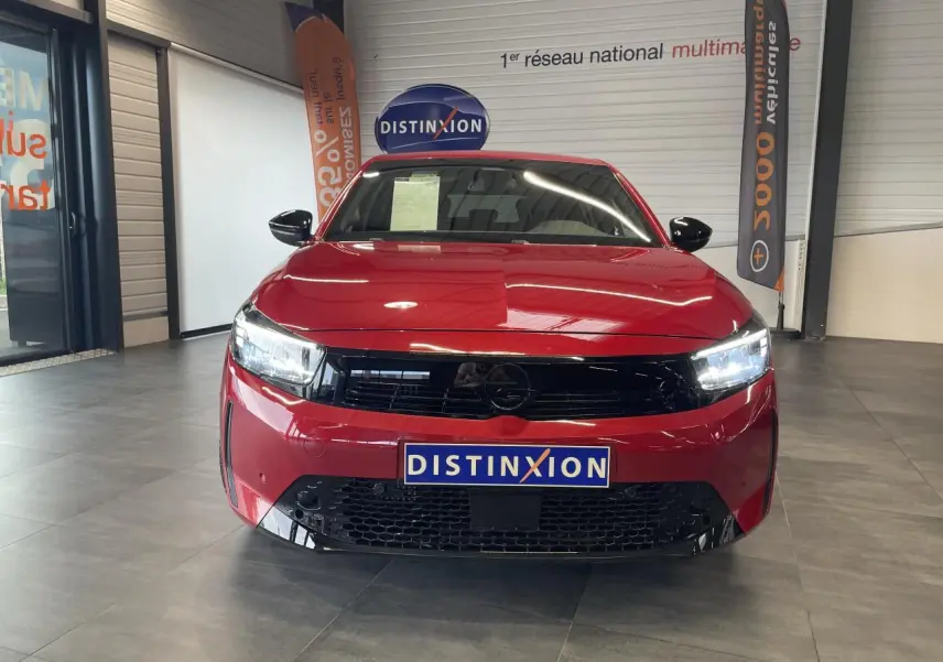 Vue avant d'une Opel Corsa rouge 2026 avec calandre noire et phares LED allumés en showroom.