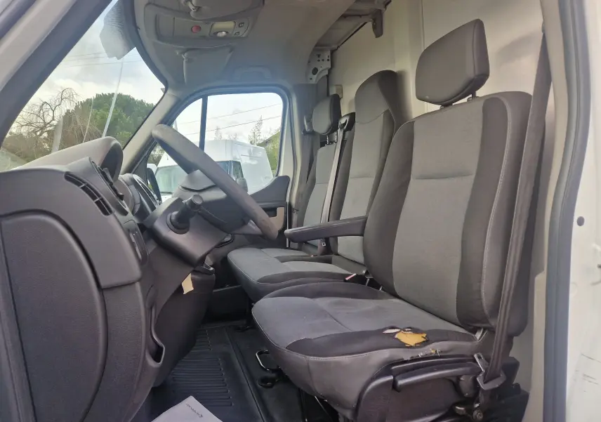 Vue intérieure côté conducteur du Renault Master Planche Cabine blanc, montrant les sièges gris avec déchirure visible sur l'assise avant.