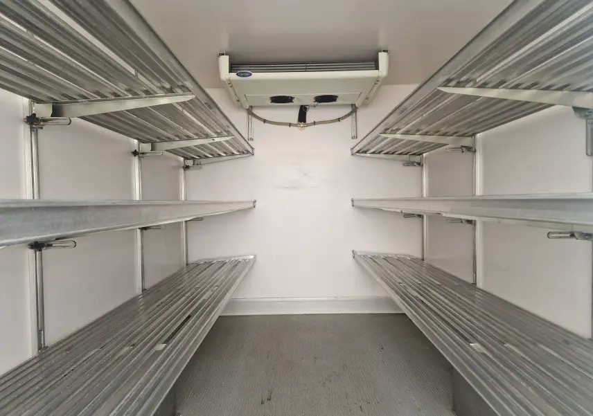 Intérieur isotherme blanc du Renault Master Plancher Cabine, vue frontale des étagères métalliques et groupe frigo Carrier au plafond.
