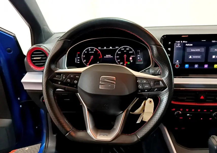 Volant cuir perforé avec surpiqûres rouges et tableau de bord numérique du SEAT Arona bleu, vue intérieure frontale.