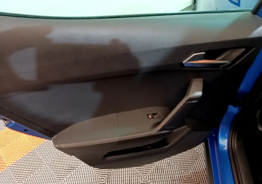 Intérieur de la porte côté gauche d'une SEAT Arona bleu 2022, avec poignée et panneau de commande noir.