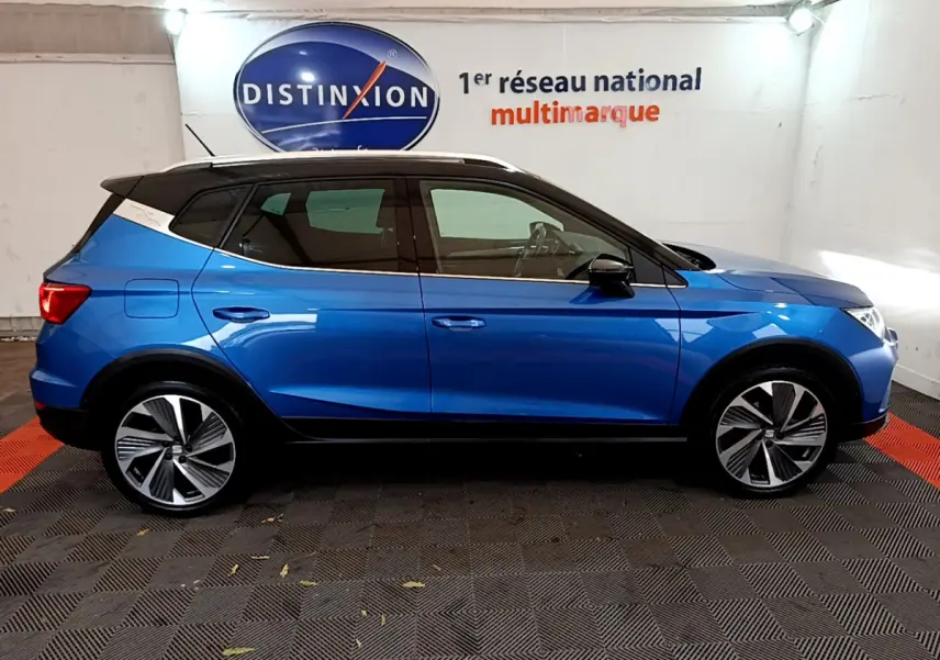 Profil côté gauche d'un SUV SEAT Arona bleu 2022 avec toit blanc et jantes alliage distinctives dans un showroom.