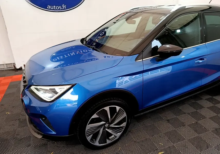 Vue 3/4 avant gauche d'un SEAT Arona bleu avec jantes alliage et rétroviseurs noirs dans un showroom.