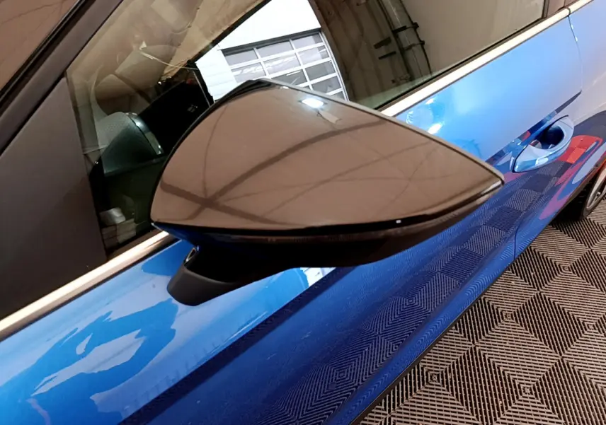 Rétroviseur côté gauche en gros plan sur SEAT Arona bleu, avec poignée de porte et reflet intérieur visibles.