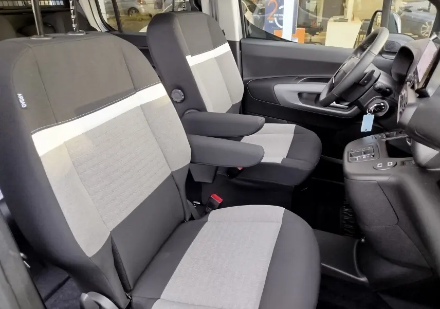 Vue intérieure côté conducteur du Citroën Berlingo 2026, sièges gris clair et foncé avec accoudoirs et volant visible.