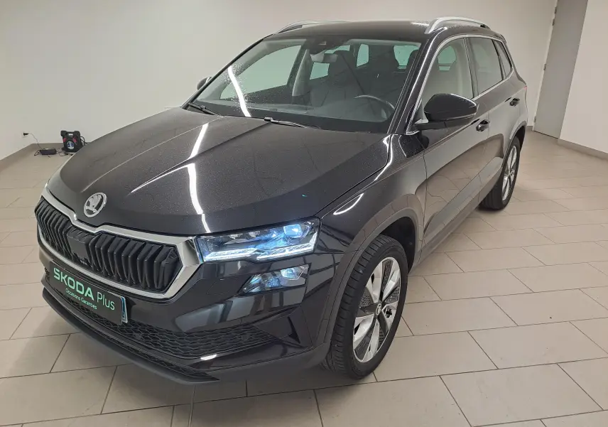 Vue 3/4 avant droite d'un Skoda Karoq noir Magic Nacré avec phares allumés dans un showroom intérieur.