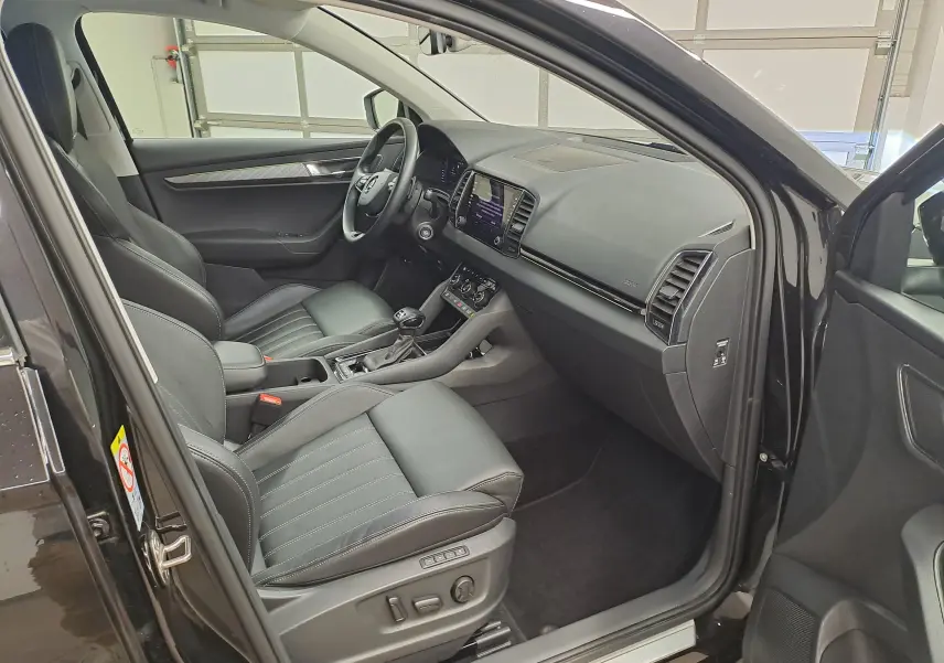 Vue intérieure côté conducteur du Skoda Karoq noir Magic Nacré 2023, avec sellerie cuir et tableau de bord moderne.