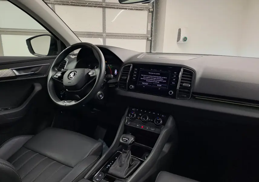 Vue intérieure côté conducteur du Skoda Karoq noir Magic Nacré 2023, avec tableau de bord et écran tactile central allumé.