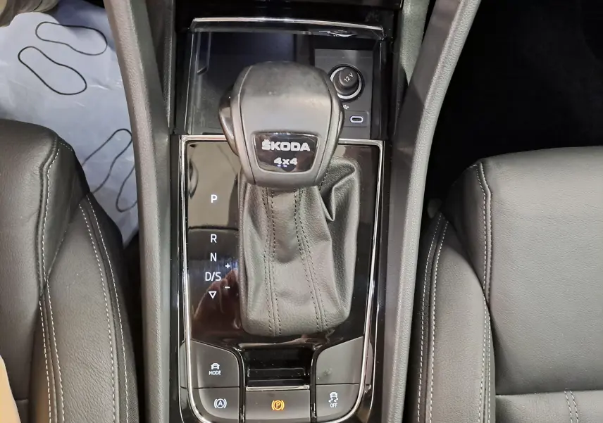 Vue rapprochée du levier de vitesse automatique noir marqué ŠKODA 4x4, entouré de sièges en cuir noir dans un Skoda Karoq 2023.