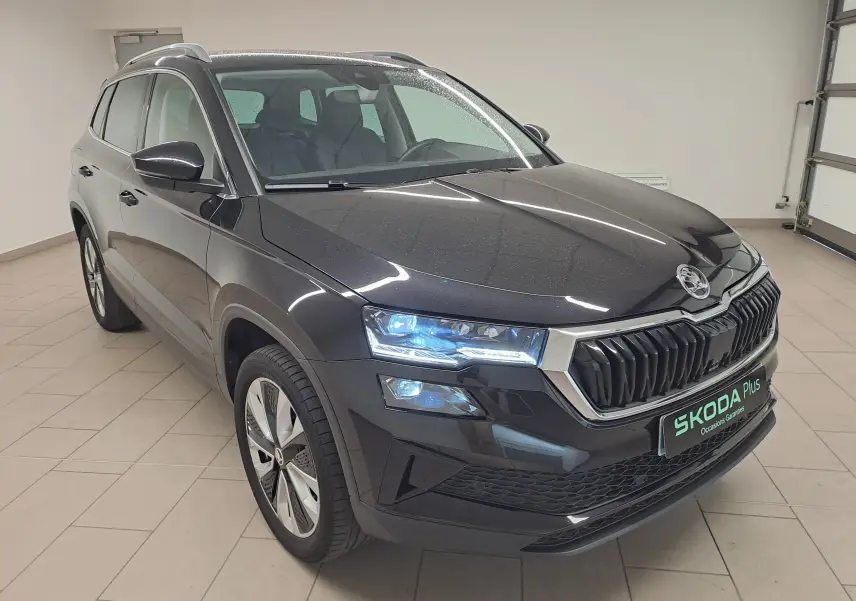 Vue 3/4 avant du Skoda Karoq noir Magic Nacré 2023 avec phares allumés et calandre chromée distinctive.