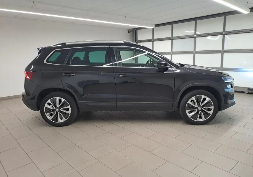 Vue de profil côté gauche d'un Skoda Karoq noir Magic Nacré 2023 avec jantes alliage et toit ouvrant panoramique.