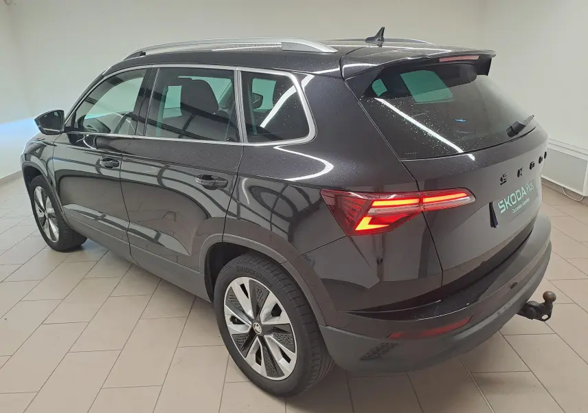 Vue 3/4 arrière droite du Skoda Karoq noir Magic Nacré avec feux allumés et crochet d'attelage escamotable visible.