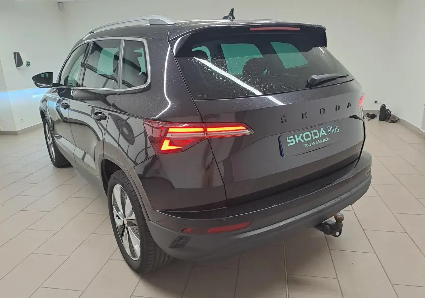 Vue 3/4 arrière droite du Skoda Karoq noir Magic Nacré avec feux allumés et crochet d'attelage escamotable visible.