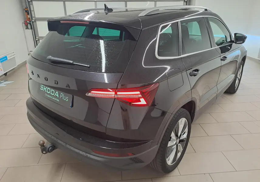 Vue 3/4 arrière droite du Skoda Karoq noir Magic Nacré 2023 avec feux allumés et crochet d'attelage escamotable.