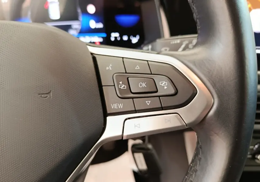 Gros plan sur le volant cuir et alu multifonctions de la Volkswagen Polo gris clair, avec commandes intégrées et affichage numérique en arrière-plan.
