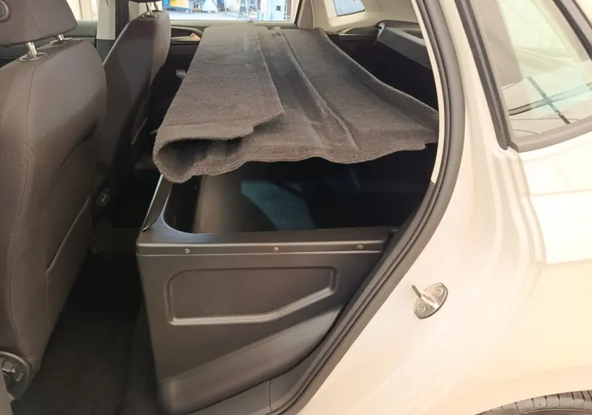 Vue intérieure côté droit du coffre ouvert d'une Volkswagen Polo gris clair avec tapis de coffre partiellement replié.