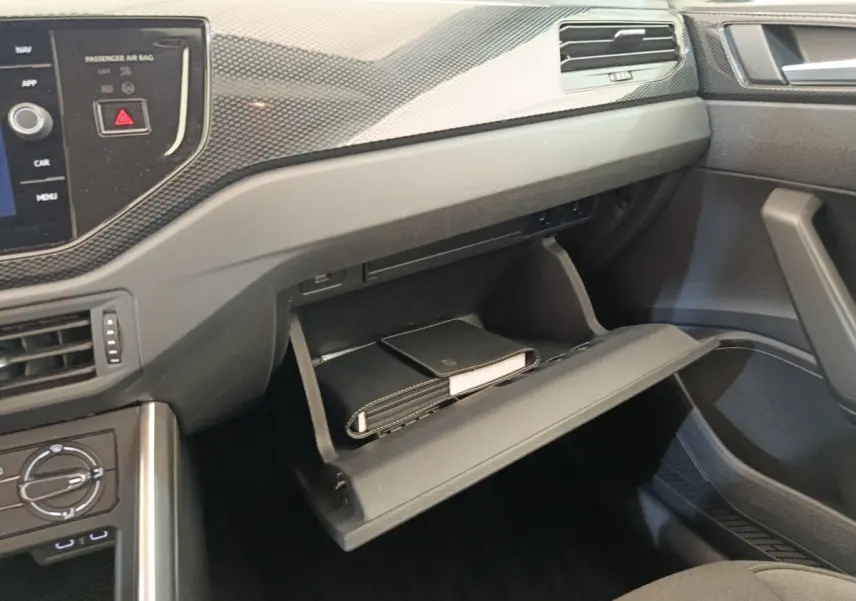 Vue intérieure côté passager de la Volkswagen Polo 2023 gris clair, boîte à gants ouverte avec documents visibles.