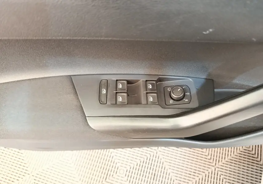 Gros plan sur les commandes des vitres et rétroviseurs électriques côté conducteur d'une Volkswagen Polo gris clair.