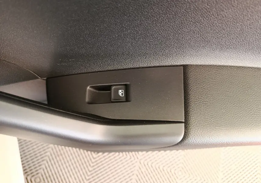 Gros plan sur le bouton de commande de lève-vitre côté conducteur dans l'habitacle noir du Volkswagen Polo gris clair.