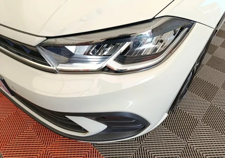 Gros plan sur le phare avant droit de la Volkswagen Polo gris clair, avec détails du pare-chocs et calandre.
