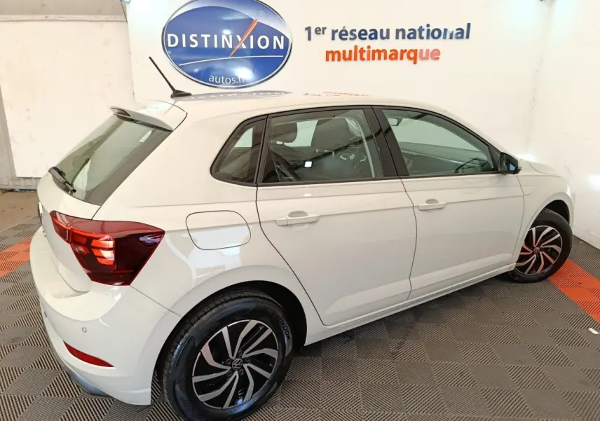 Vue 3/4 arrière droite d'une Volkswagen Polo gris clair avec jantes alliage noires et rouges en intérieur showroom.
