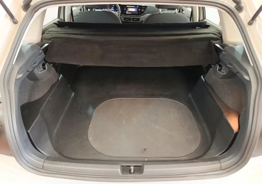 Coffre ouvert vu de l'arrière d'une Volkswagen Polo gris clair, avec cache-bagages déployé et intérieur noir.