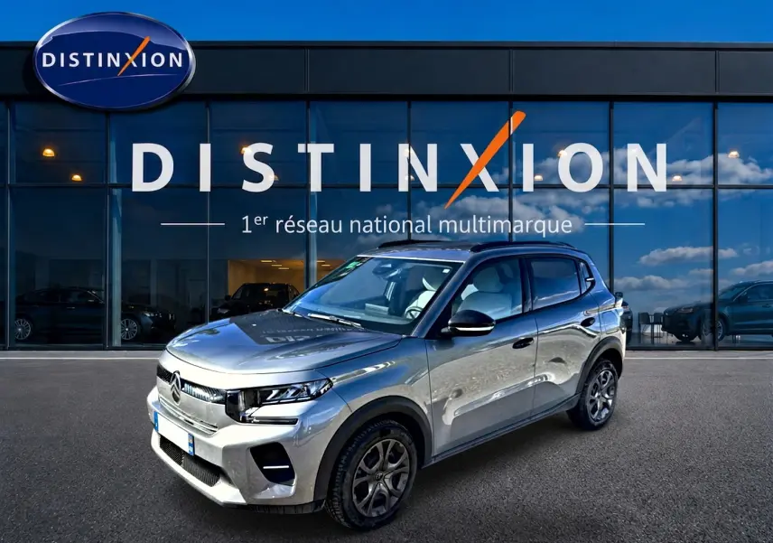 Vue 3/4 avant d'une Citroën C3 gris mercure garée devant une vitrine avec logo Distinxion.