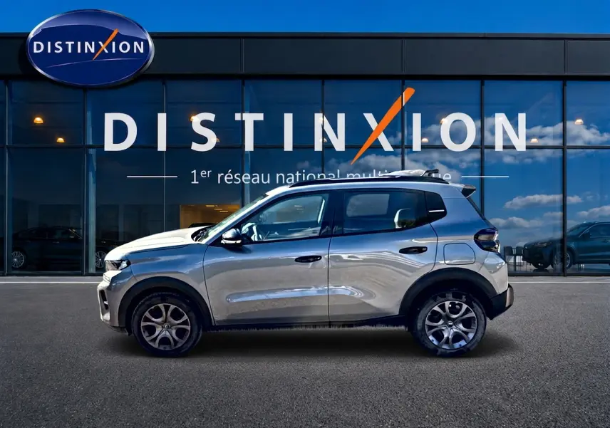Profil droit d'une Citroën C3 1.2 turbo 100 essence gris mercure avec jantes alu, stationnée devant une vitrine Distinxion.