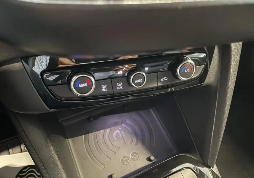 Gros plan sur la console centrale de l'Opel Corsa gris, montrant la commande de climatisation et le chargeur sans fil.