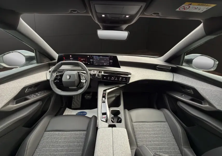 Vue intérieure avant du Peugeot 3008 2025 hybride, tableau de bord gris clair et sièges cuir noir avec tissu gris.