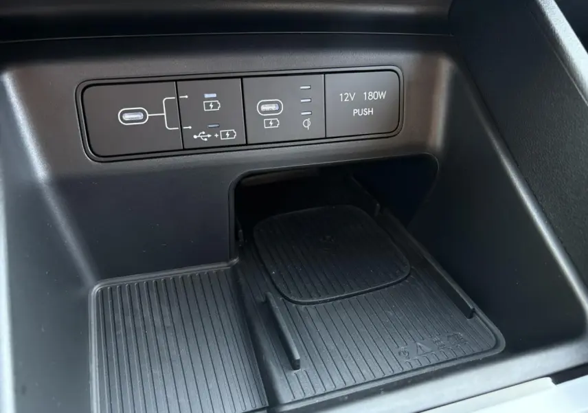 Gros plan sur la console centrale noire du Hyundai Tucson 2025 avec ports USB, prise 12V et chargeur sans fil.