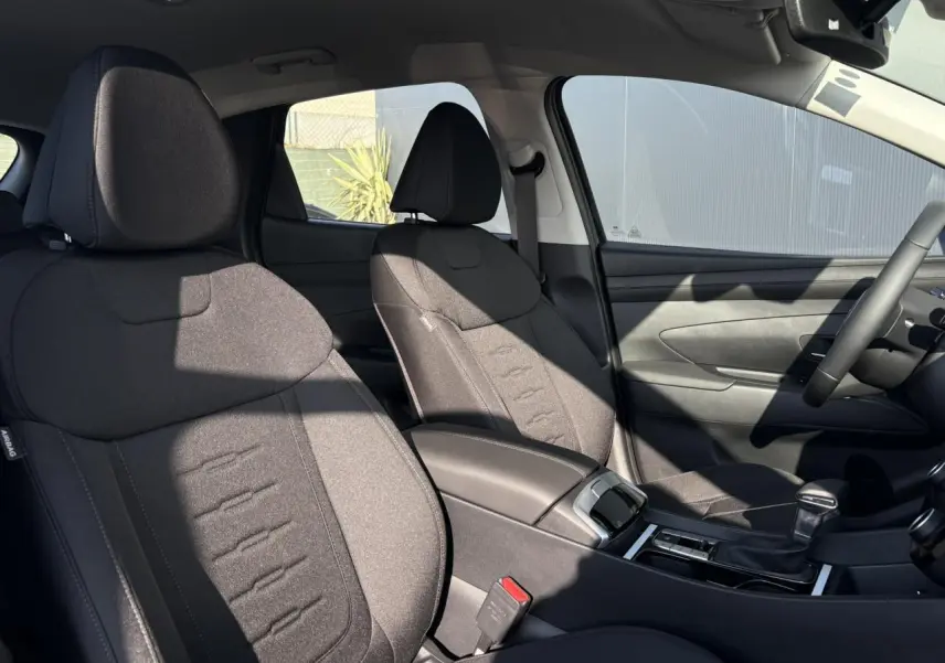 Intérieur du Hyundai Tucson 2025 vu côté droit, sièges tissu gris foncé et console centrale avec levier de vitesses.