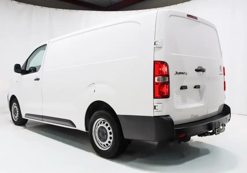 Vue 3/4 arrière droite d'un fourgon Citroën Jumpy blanc avec attelage et porte latérale coulissante.