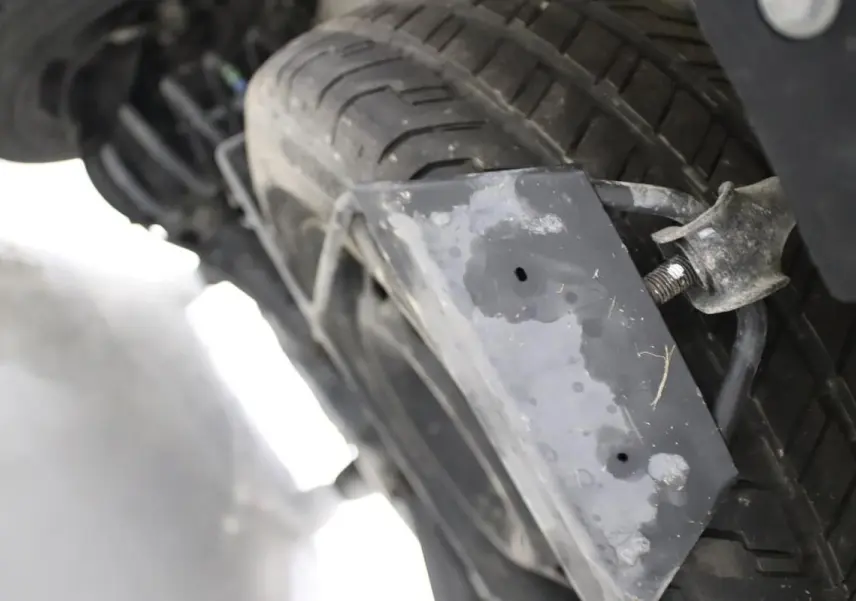 Gros plan sur la roue de secours sous le châssis d’un Citroën Jumpy blanc, montrant le support métallique usé.