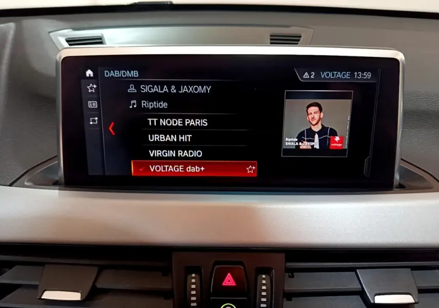 Écran tactile central du tableau de bord du BMW X1 noir, affichant la liste des radios DAB avec sélection sur Voltage dab+.