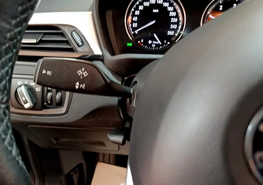 Gros plan sur le volant cuir et le combiné d'instruments du BMW X1 noir, avec commandes et tableau de bord visibles.