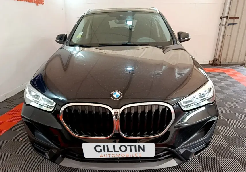 Vue frontale d'un BMW X1 noir 2020 avec calandre double haricot et phares LED allumés dans un showroom.