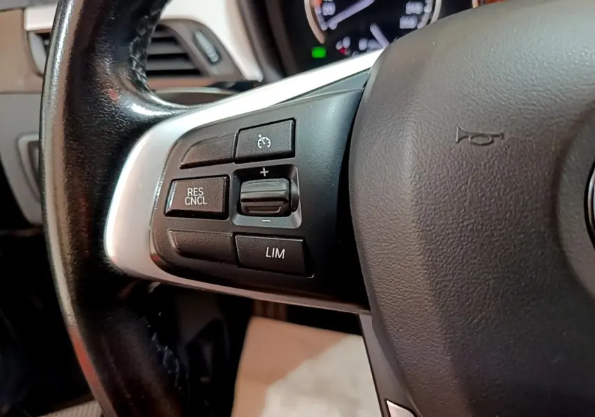 Gros plan sur les commandes de régulateur de vitesse du volant cuir noir de la BMW X1 sDrive16d 2020.